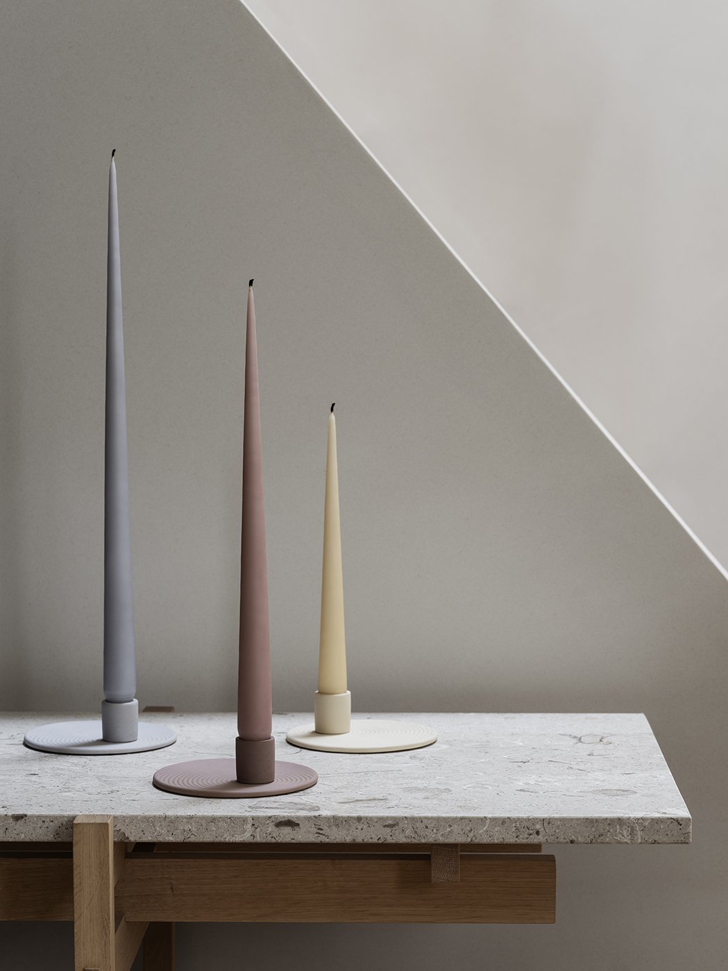 Elegant tapered candles in pastel colors displayed on a minimalist stone surface.