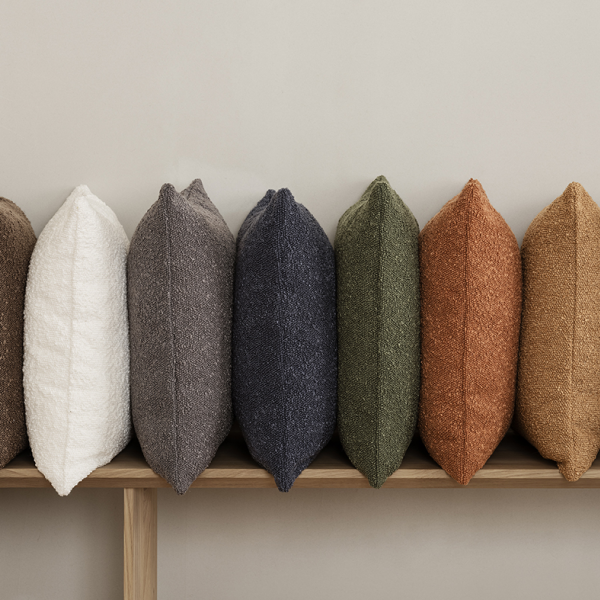 Stylische dekorative Kissen in verschiedenen Farben, die auf einem Holzregal angeordnet sind.