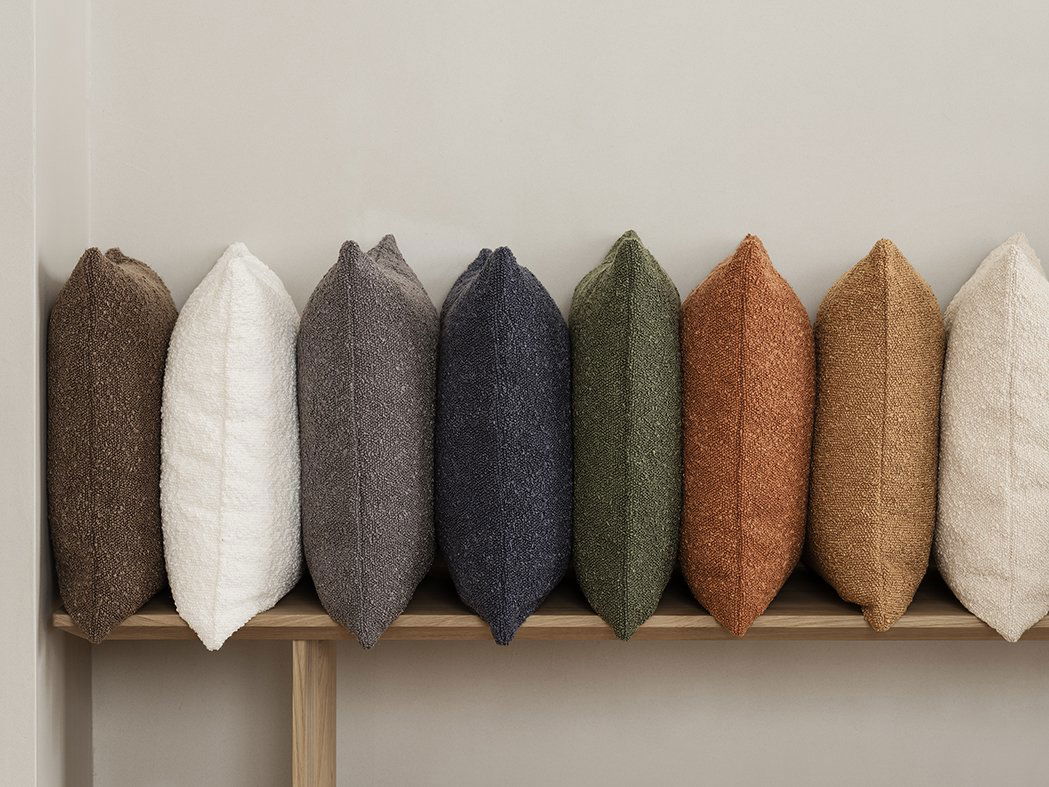 Stylische dekorative Kissen in verschiedenen Farben, die auf einem Holzregal angeordnet sind.