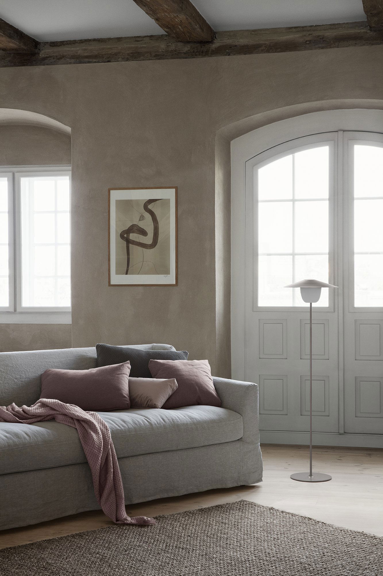 Cozy living room with a modern artwork, soft pillows, and natural light from large windows.