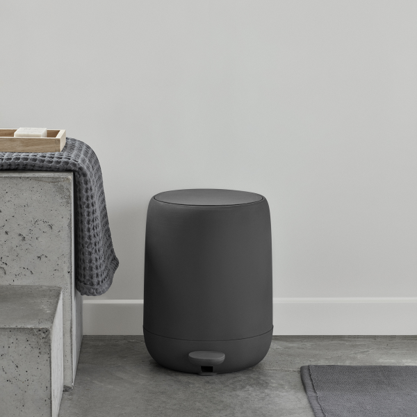 Modern black bathroom trash can beside a concrete bench in a minimalist setting.