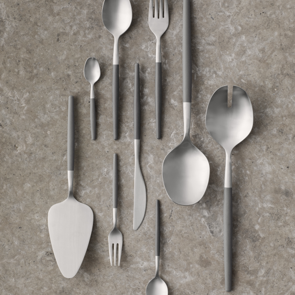 Assorted modern stainless steel cutlery arranged on a textured gray surface.