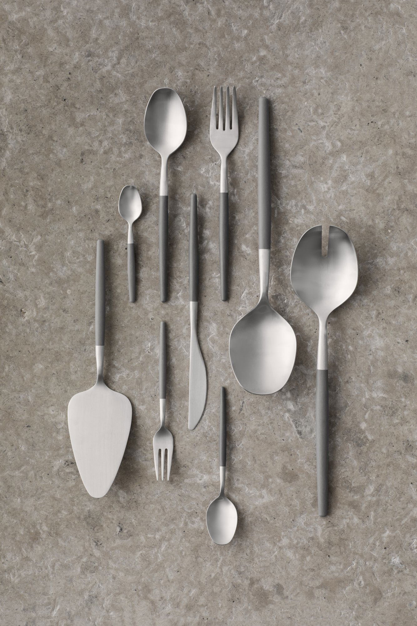 Assorted modern stainless steel cutlery arranged on a textured gray surface.