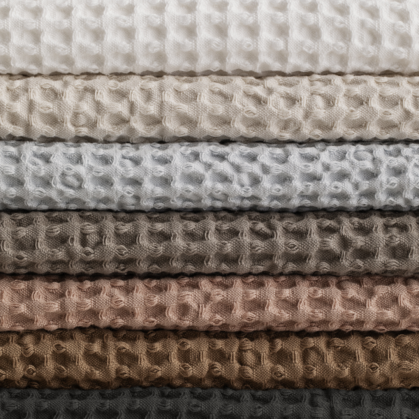 Stack of textured waffle fabrics in various neutral colors for home decor.
