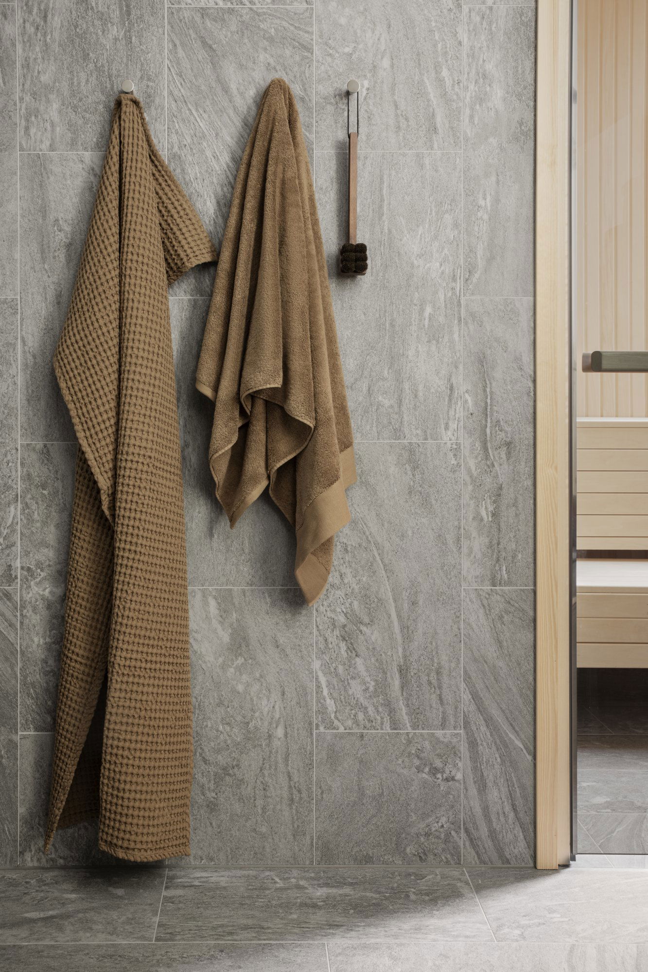 Cozy brown towels hanging on a textured gray bathroom wall next to a sauna.
