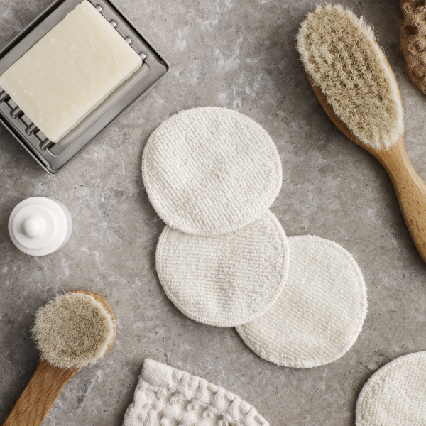 Natural skincare tools including reusable cotton pads, brushes, and soap on a textured surface.