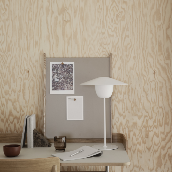 Modern workspace featuring minimalist decor, a lamp, and pinned notes on a soft wood backdrop.