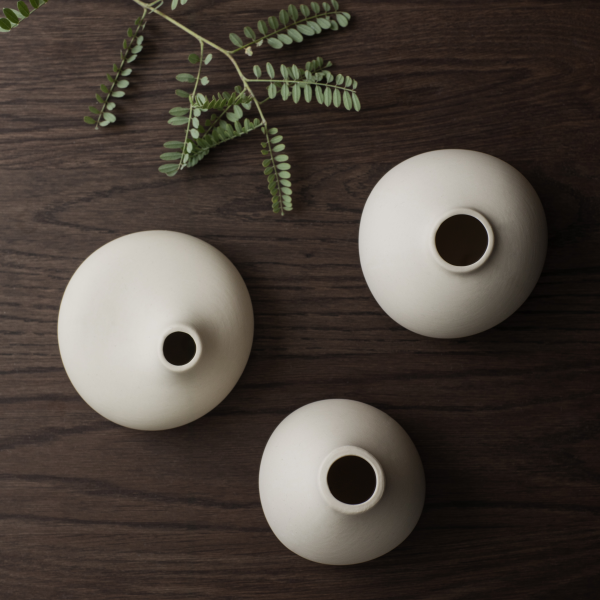 Minimalist ceramic vases arranged on a dark wooden surface with green leaves.