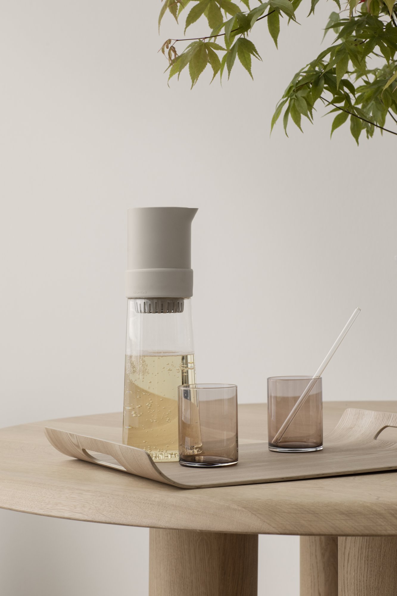 Elegante Glaskaraffe für Wasser mit zwei passenden braunen Gläsern auf einem Holztablett.