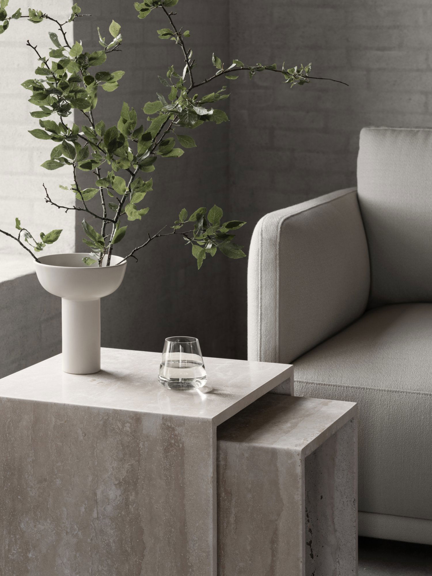 Modern living room scene featuring a minimalist vase, greenery, and a stylish glass on a marble table.