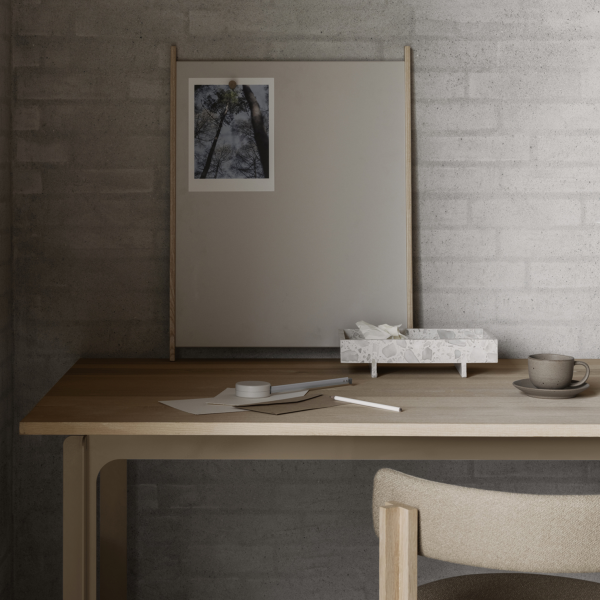 Minimalistischer Arbeitsplatz mit einem Holztisch, einem Spiegel und Schreibwaren vor einem neutralen Hintergrund.