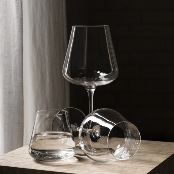 Elegante Glassarrangements mit einem hohen Weinglas und zwei Bechern auf einer Holzoberfläche.