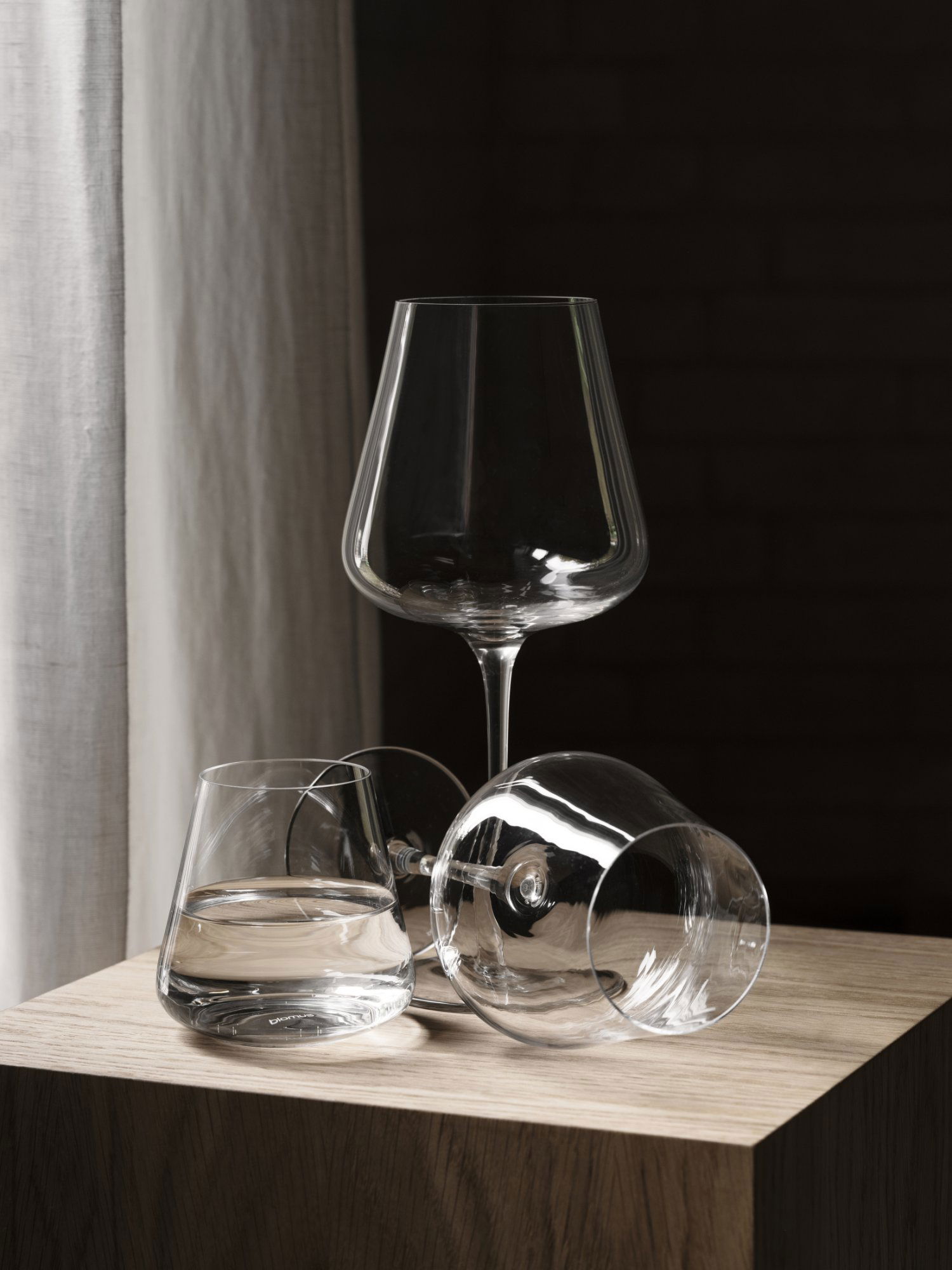 Elegante Glassarrangements mit einem hohen Weinglas und zwei Bechern auf einer Holzoberfläche.