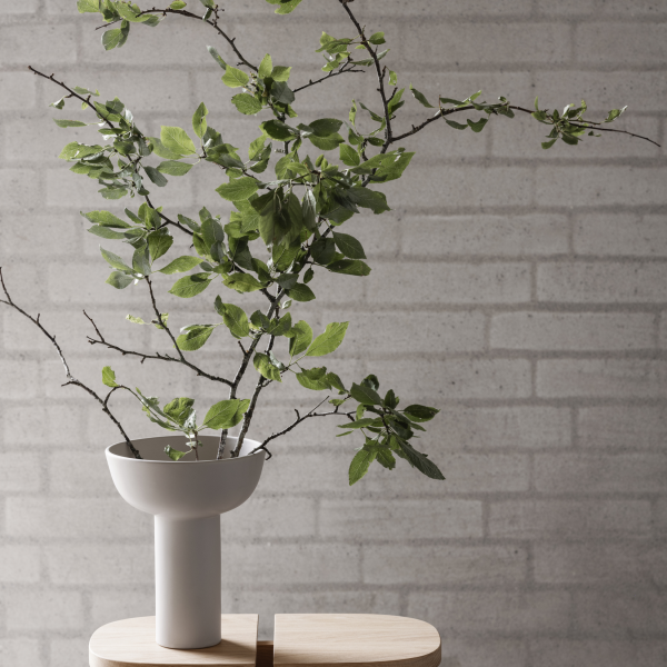 Minimalistic vase with branches and fresh green leaves against a textured brick wall.