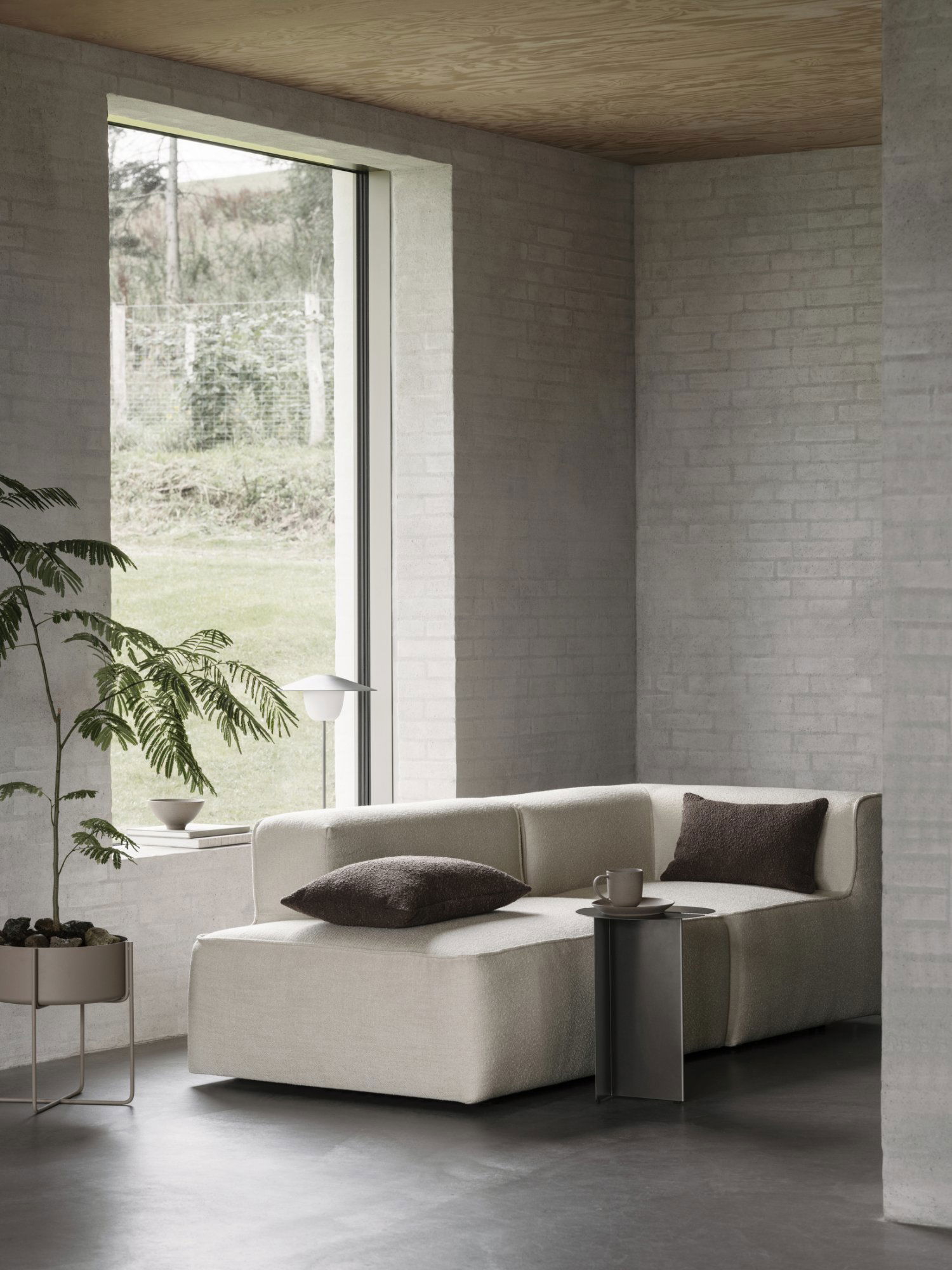 Modernes Wohnzimmer mit einem stilvollen beigen Sofa, minimalistischer Dekoration und großen Fenstern.