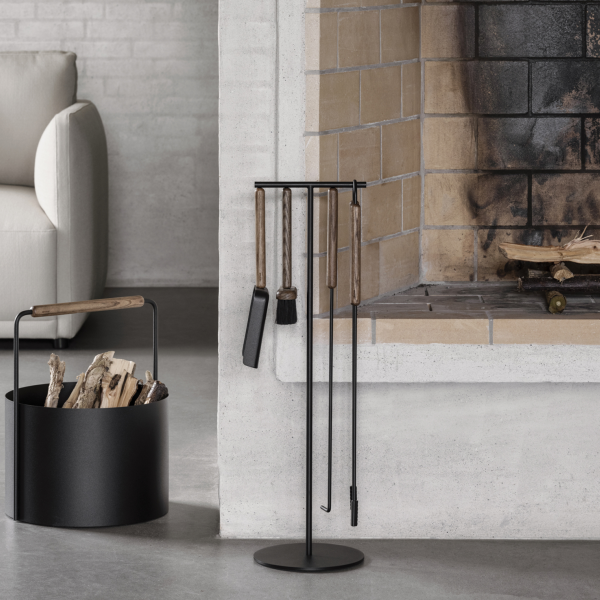 Modern fireplace tools displayed near a cozy stone fireplace and log holder.