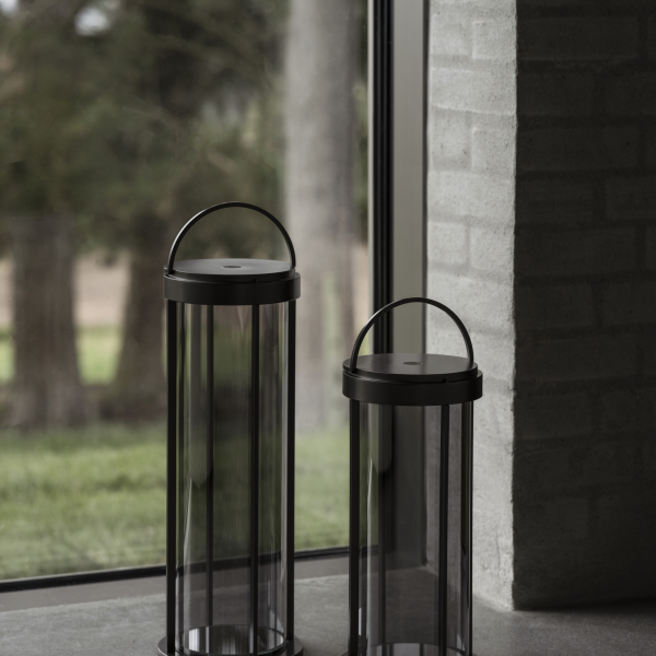 Moderne Glaslaternen mit Metallgriffen neben einem Fenster, das eine natürliche Landschaft zeigt.