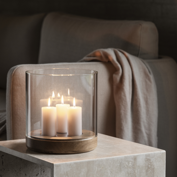 Gemütliche Wohnzimmer-Szene mit einem Glas-Teelichthalter und fünf brennenden Kerzen auf einem Tisch.