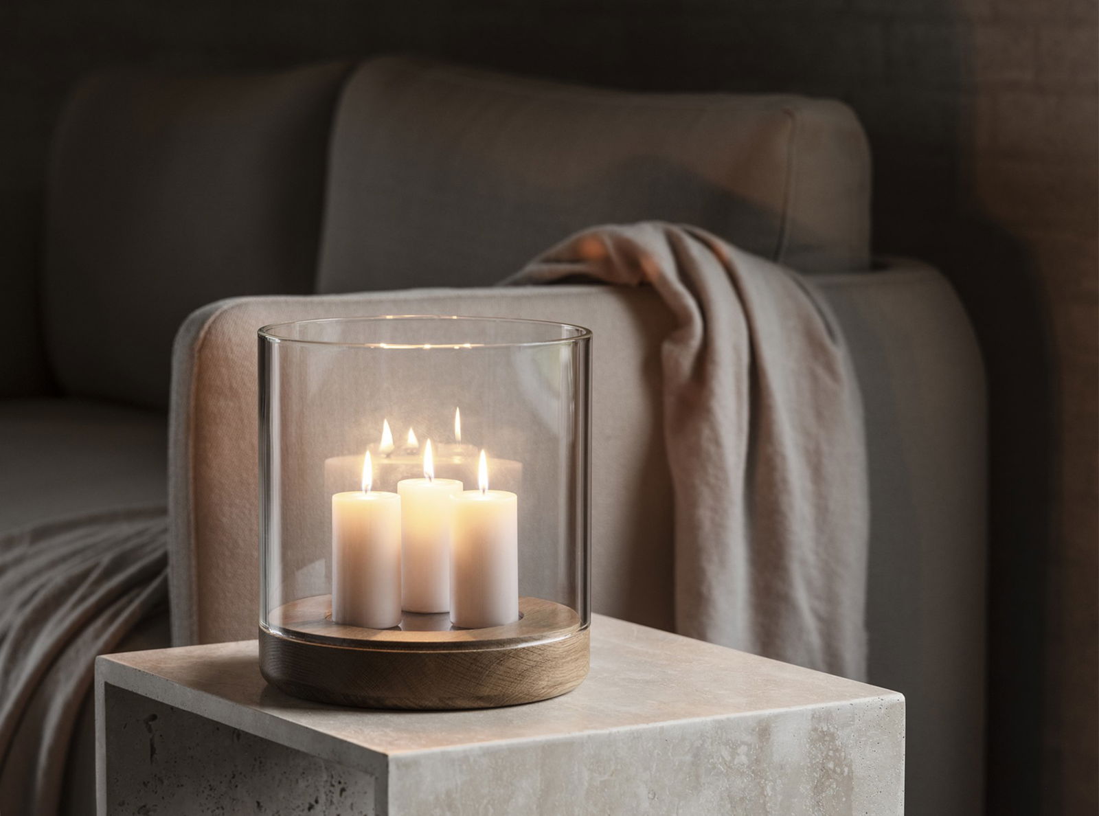 Gemütliche Wohnzimmer-Szene mit einem Glas-Teelichthalter und fünf brennenden Kerzen auf einem Tisch.