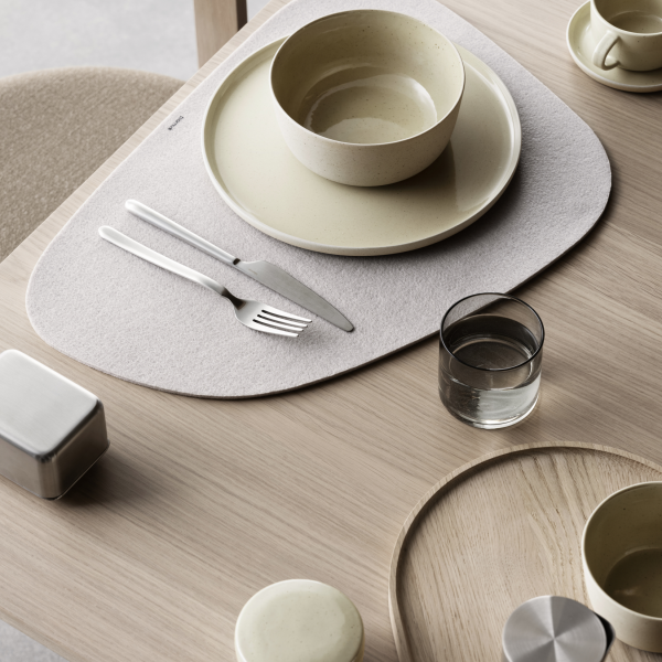 Moderne Essbereich mit minimalistischem Geschirr und stilvoller Tischunterlage auf einem Holztisch.