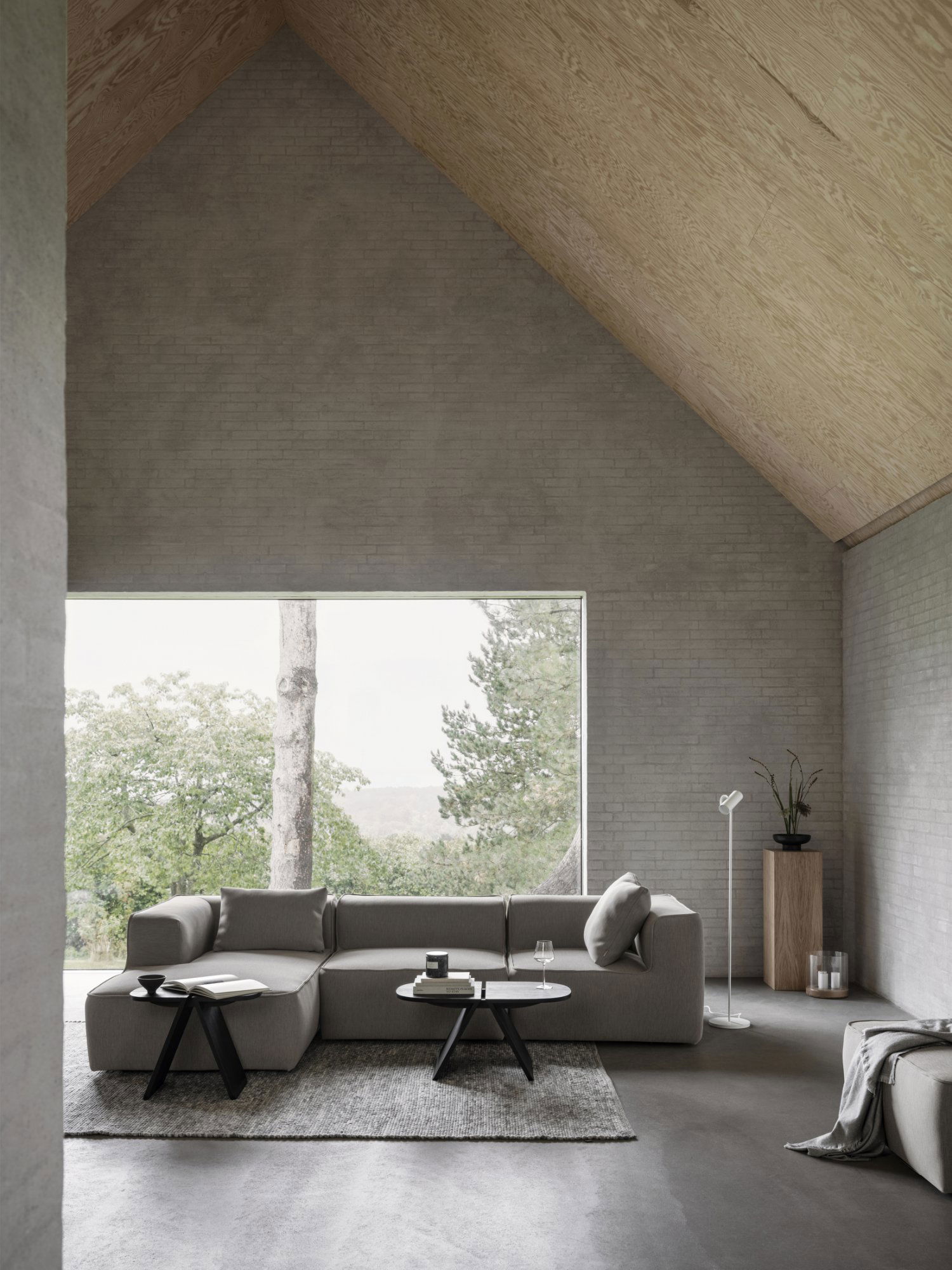 Modern living room with a gray sectional sofa and large window overlooking greenery.