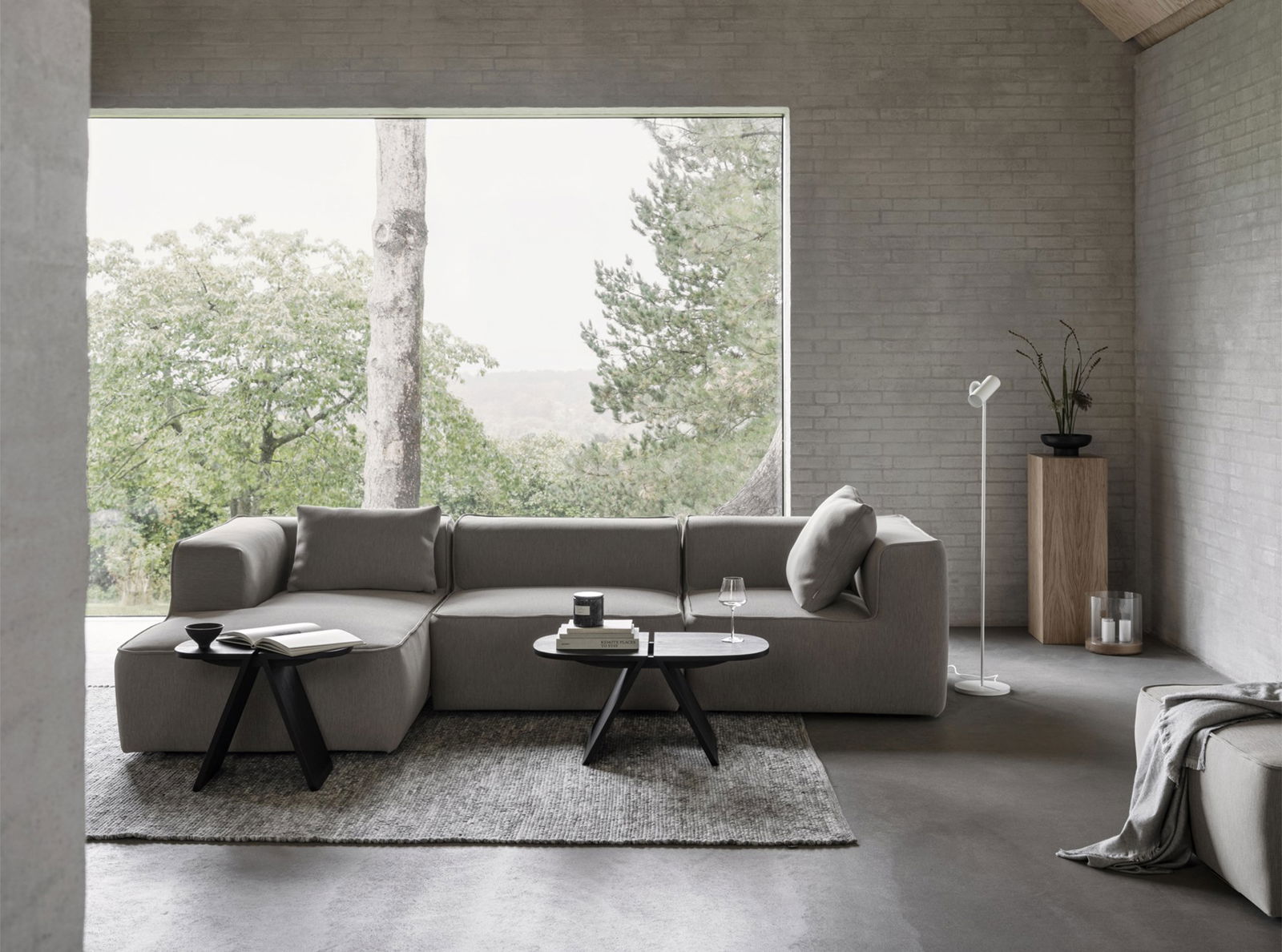 Modernes Wohnzimmer mit einem grauen Sofa, minimalistischer Dekoration und großem Fenster mit Blick auf die Natur.
