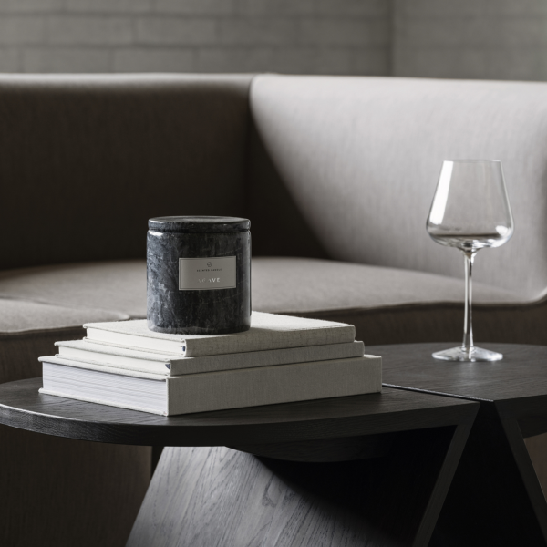 Stylish candle on stacked books beside a glass of wine and modern sofa in a cozy living space.