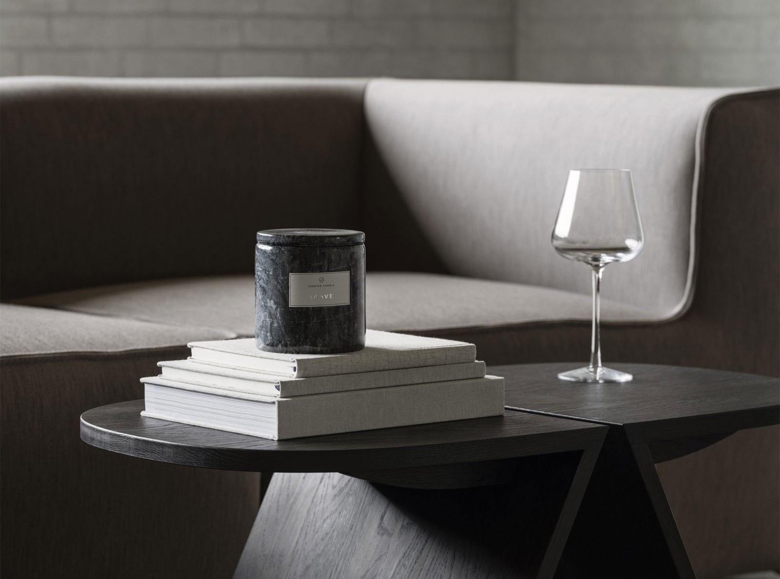 Stylish candle on stacked books beside a glass of wine and modern sofa in a cozy living space.