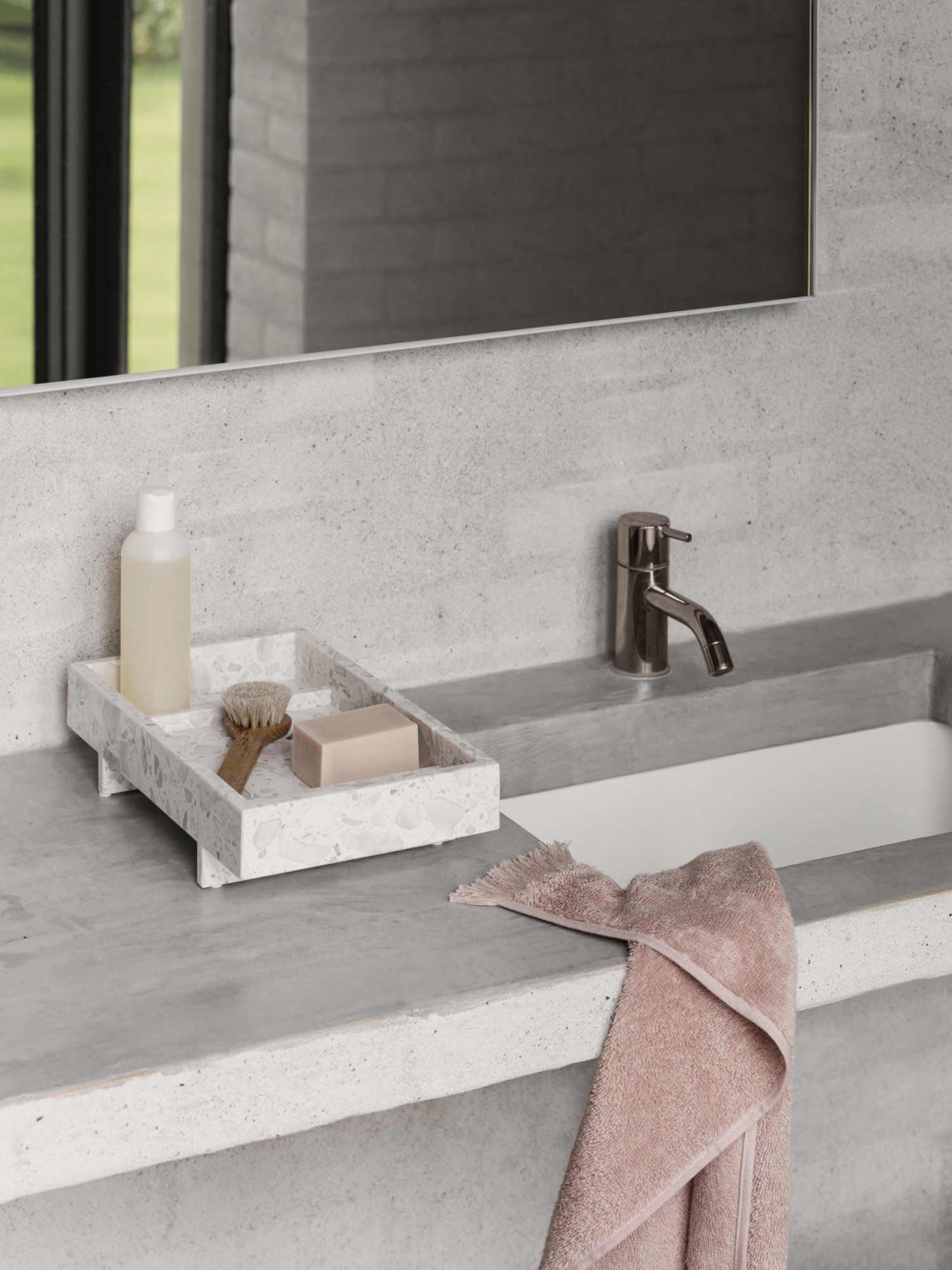 Modern bathroom sink with a stone tray holding soap, a brush, and a bottle, complemented by a towel.