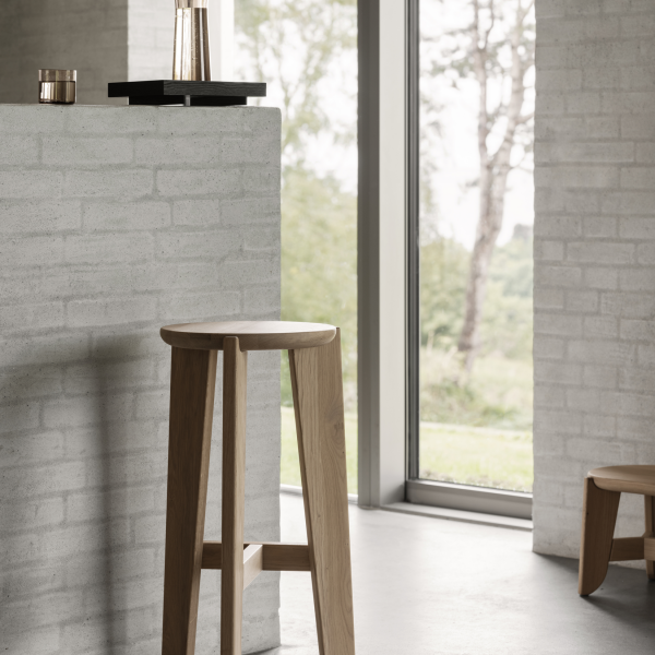 Modern wooden stool in a bright, minimalist interior with large windows.