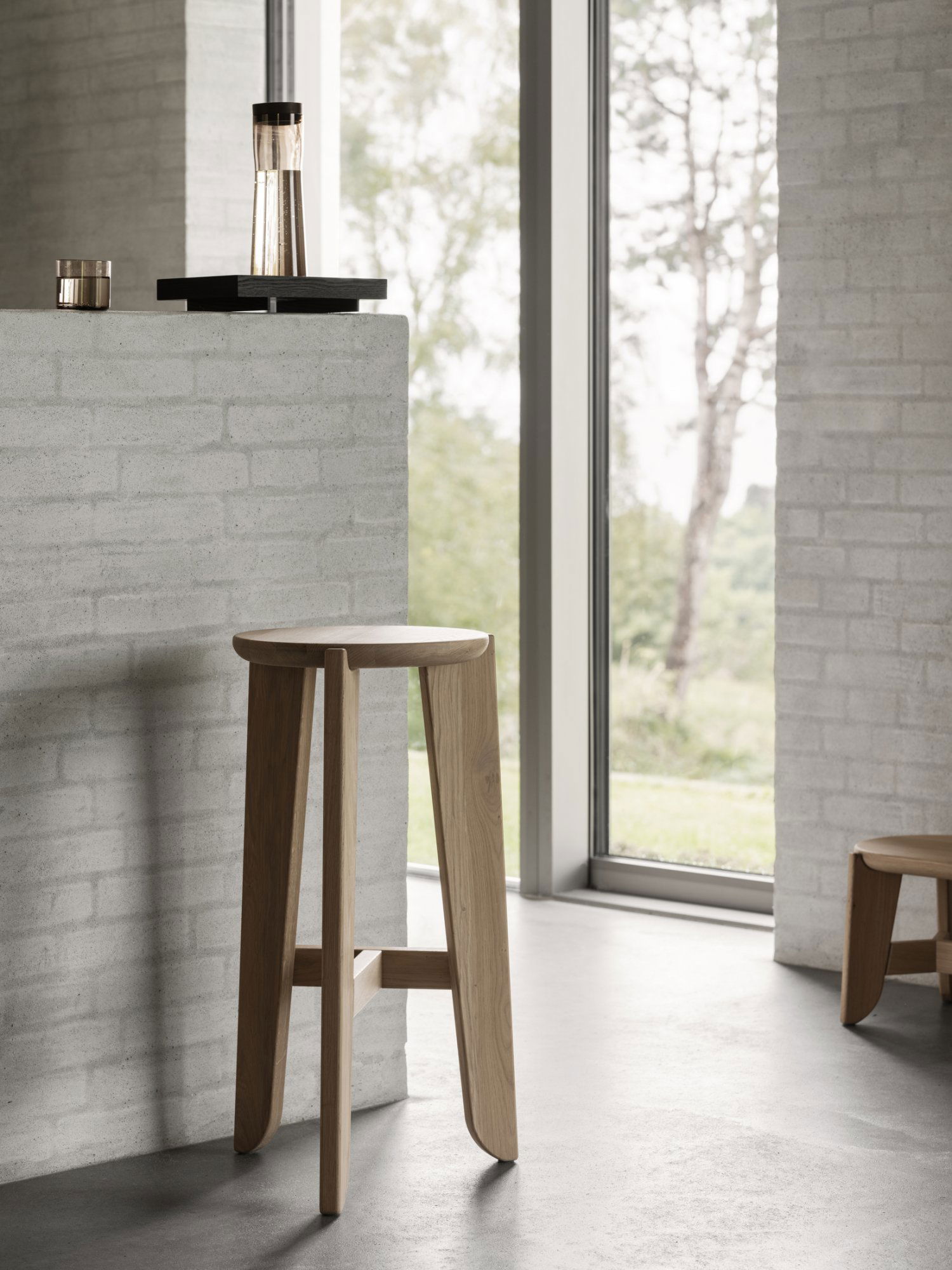 Modern wooden stool in a bright, minimalist interior with large windows.