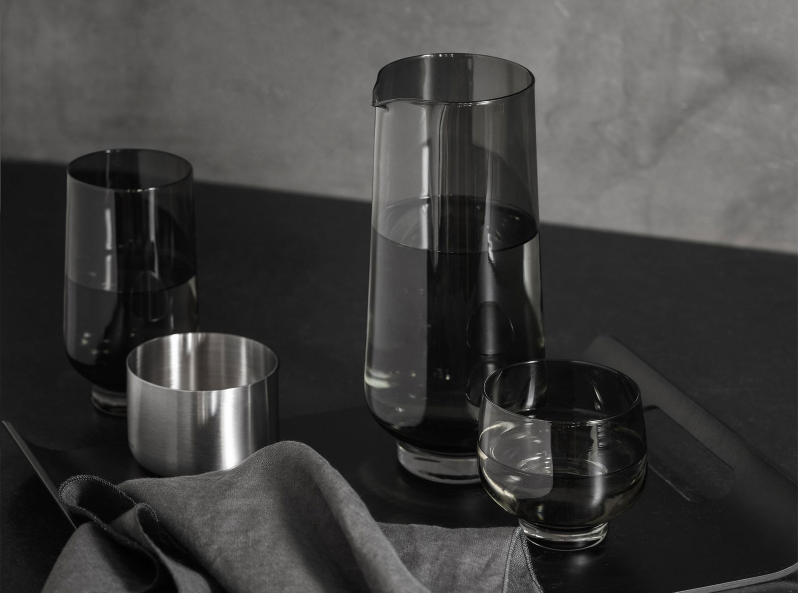 Elegantes Glasgeschirrset mit einer Kanne und Gläsern auf einem stilvollen schwarzen Tisch.
