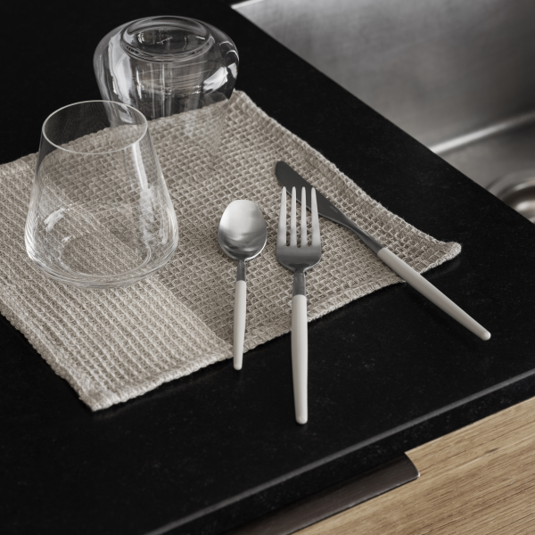 Modern dining setup with cutlery, glassware, and a textured placemat on a dark countertop.