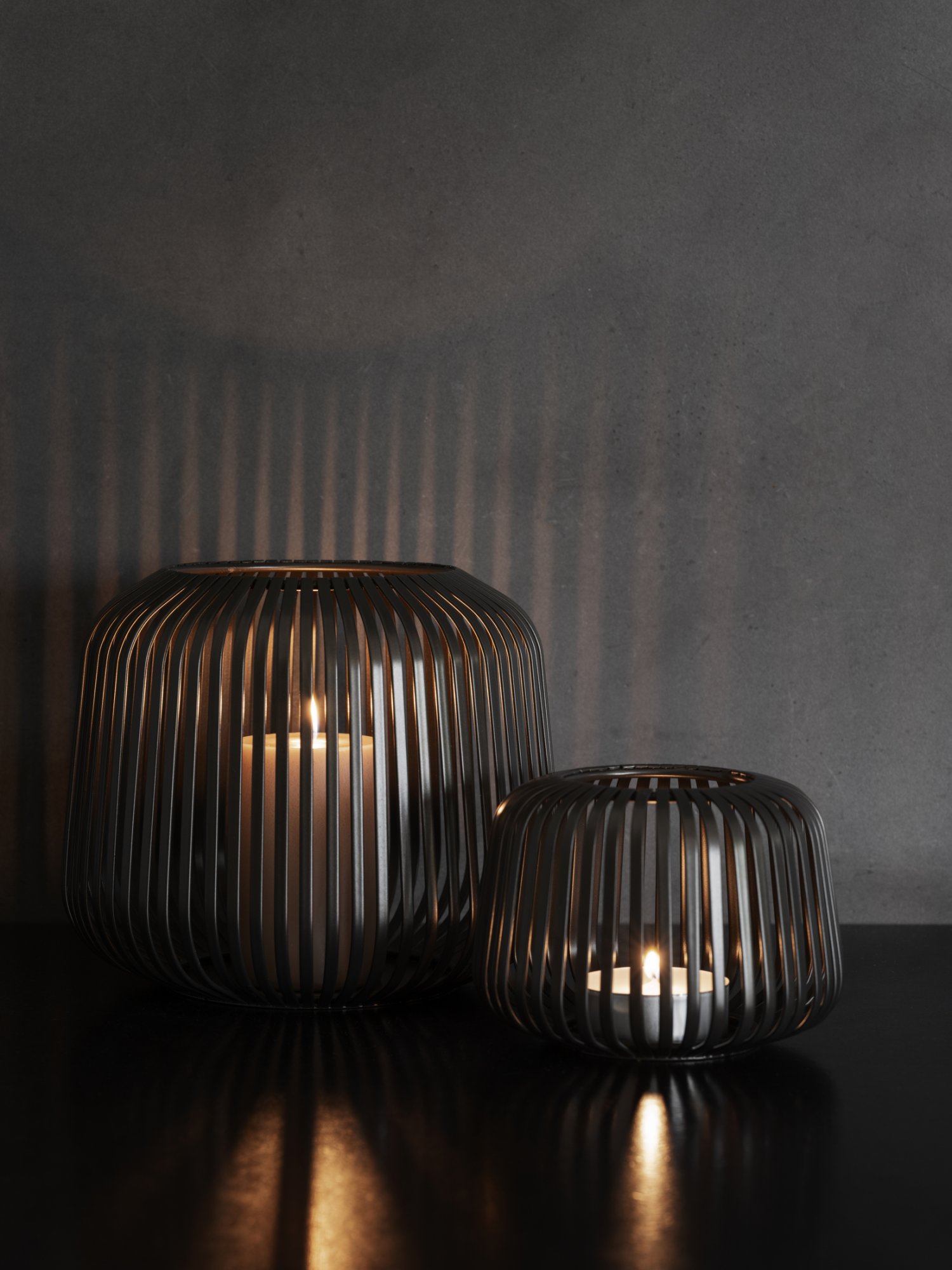 Elegante Metallkerzenhalter, die warme Schatten auf einem dunklen Wandhintergrund werfen.
