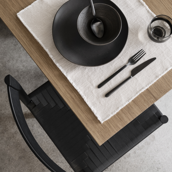 Elegante Tischeinstellung mit schwarzem Geschirr auf einem Tisch und Stuhl aus naturbelassenem Holz.