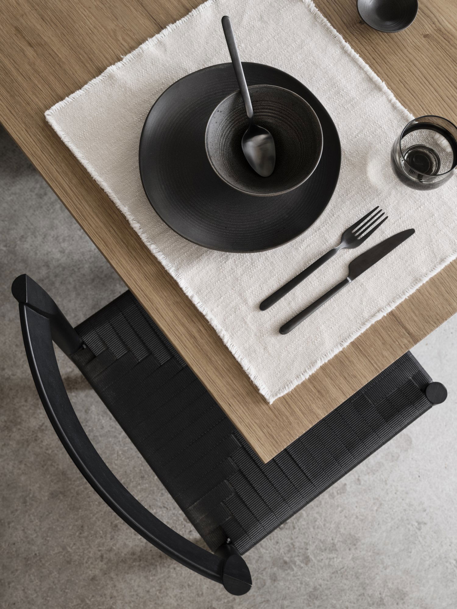 Elegante Tischeinstellung mit schwarzem Geschirr auf einem Tisch und Stuhl aus naturbelassenem Holz.