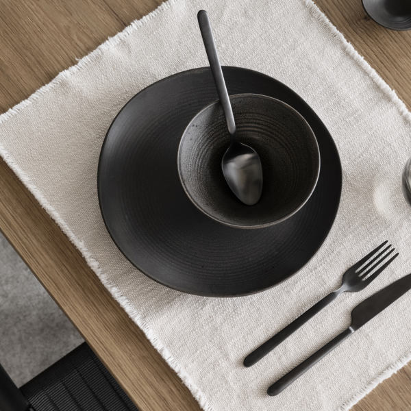 Elegantes schwarzes Geschirrset auf einem strukturierten Leinen-Tischset für ein minimalistisches Ess-Erlebnis.