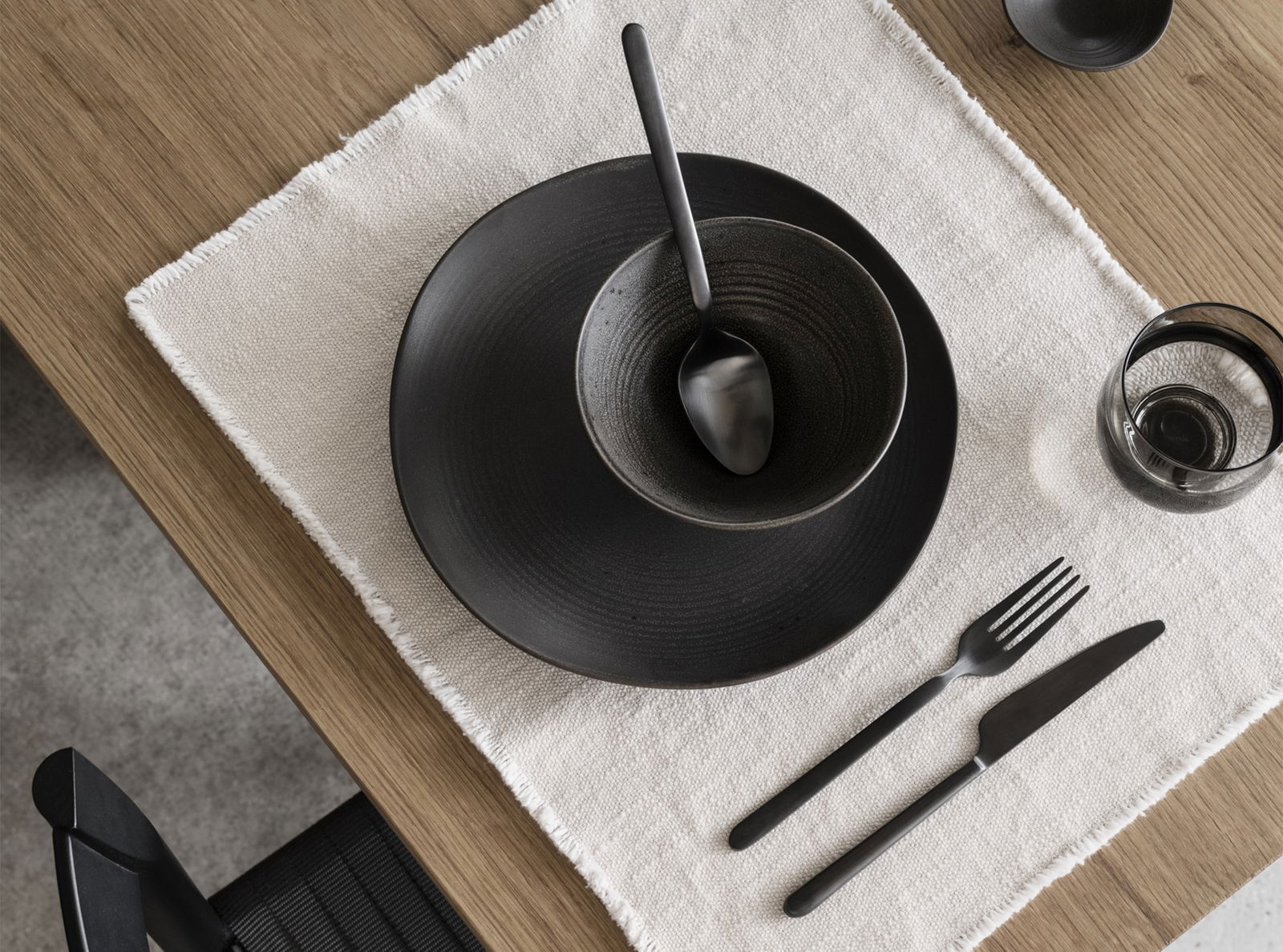 Elegantes schwarzes Geschirrset auf einem strukturierten Leinen-Tischset für ein minimalistisches Ess-Erlebnis.