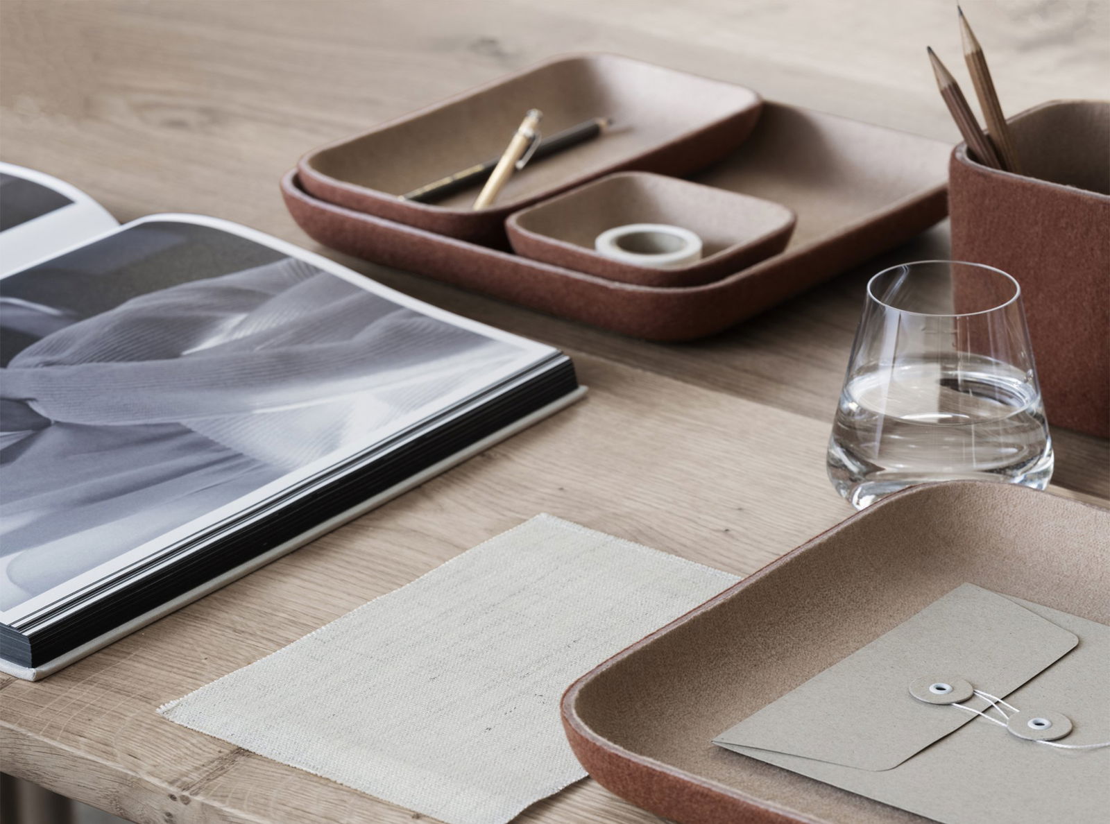 Minimalistischer Arbeitsplatz mit Organizern, Notizbuch und einem Glas Wasser auf einem Holztisch.