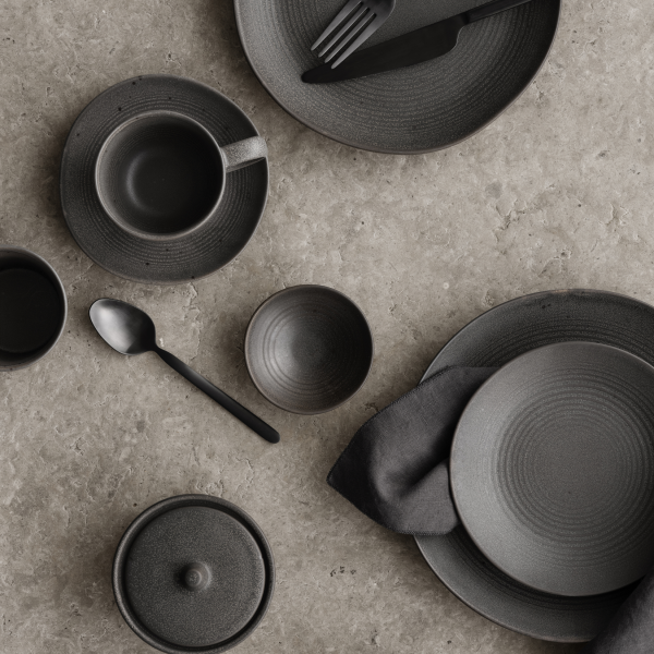 Stylisches schwarzes Keramikteller-Set angeordnet auf einer strukturierten grauen Oberfläche.