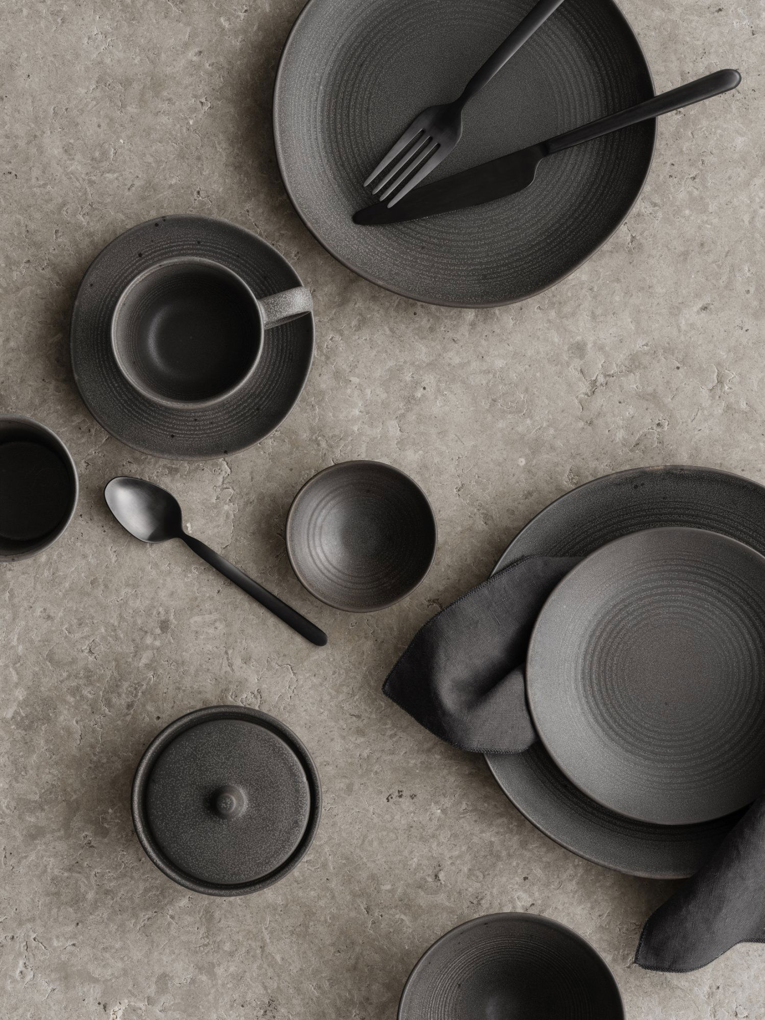 Stylisches schwarzes Keramikteller-Set angeordnet auf einer strukturierten grauen Oberfläche.