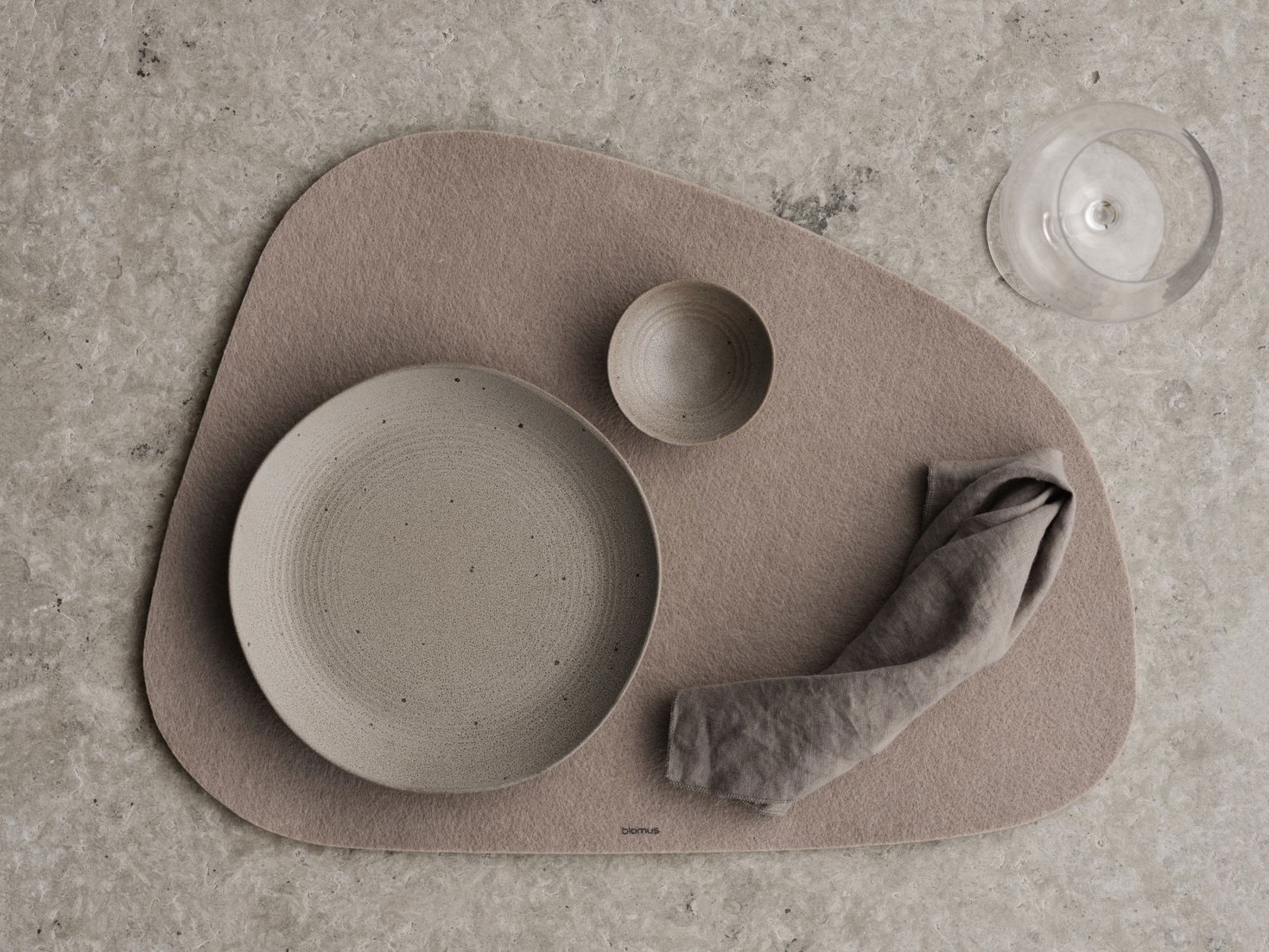 Stylisches Essensarrangement mit Keramiktellern, -schüsseln und einer Stoffserviette auf einem strukturierten Platzset.