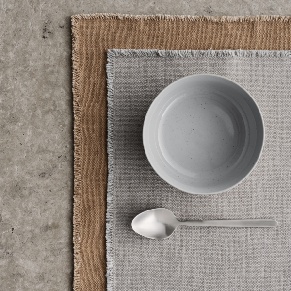 Minimalistische Tischdekoration mit einer hellen Schüssel, einem Löffel und strukturierten Platzsets.