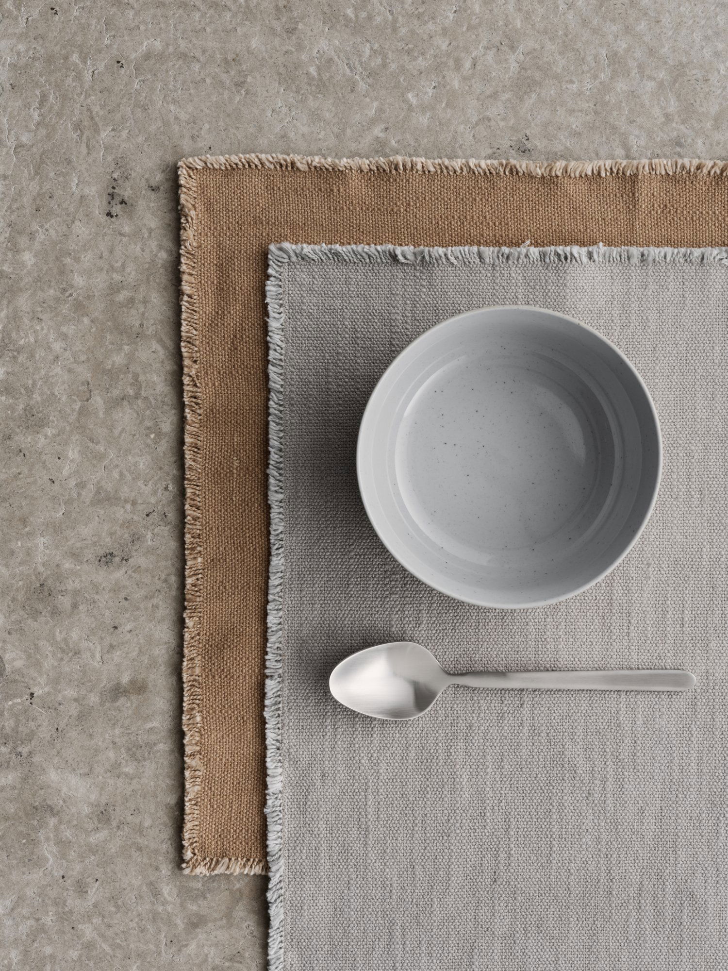 Minimalistische Tischdekoration mit einer hellen Schüssel, einem Löffel und strukturierten Platzsets.