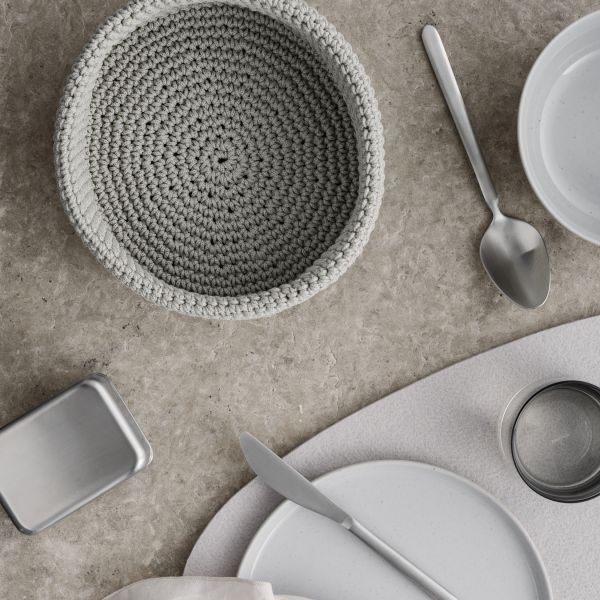 Stylish table setting with a gray crochet bowl and elegant dishware on a textured surface.