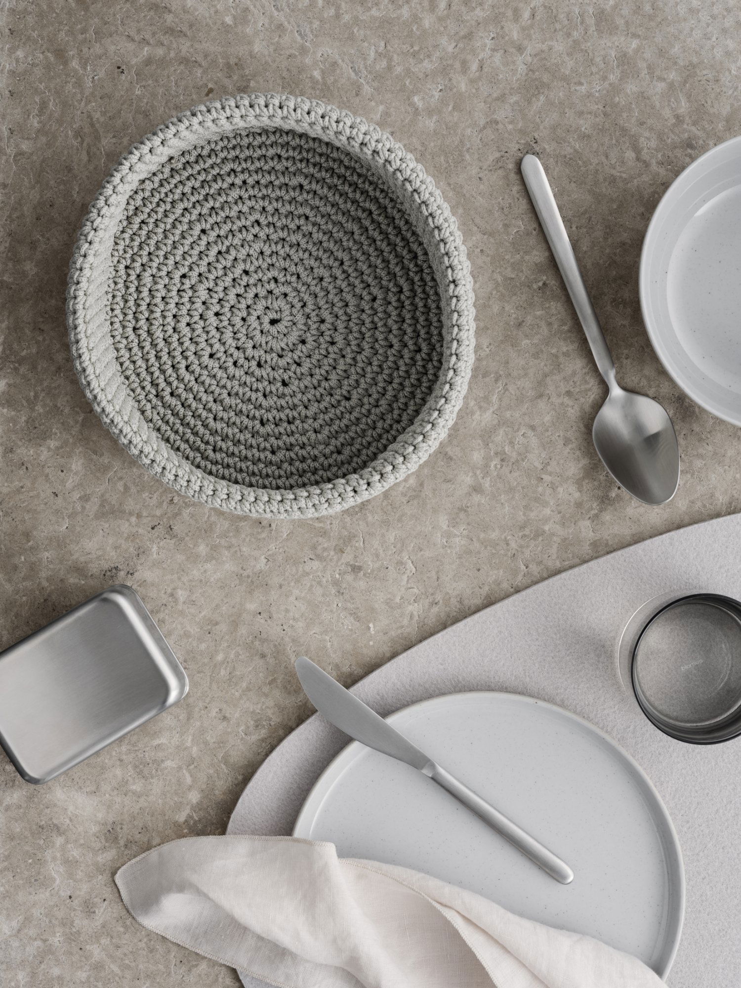 Stylish table setting with a gray crochet bowl and elegant dishware on a textured surface.