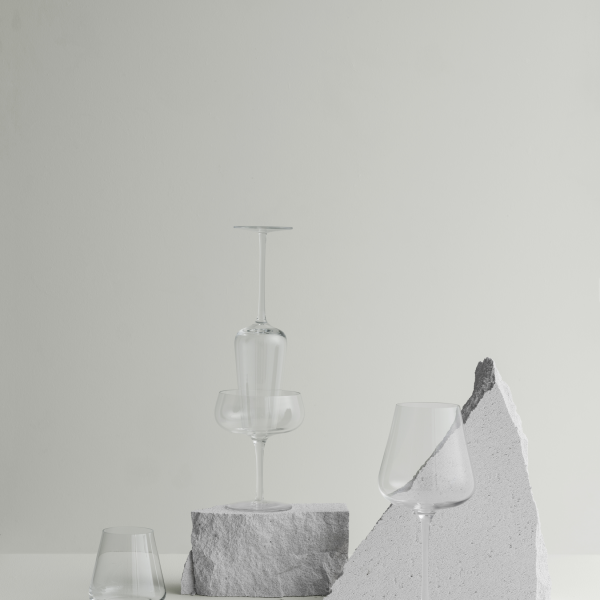Elegantes Glasgeschirr, kunstvoll auf strukturierten Steinoberflächen vor einem minimalistischen Hintergrund arrangiert.