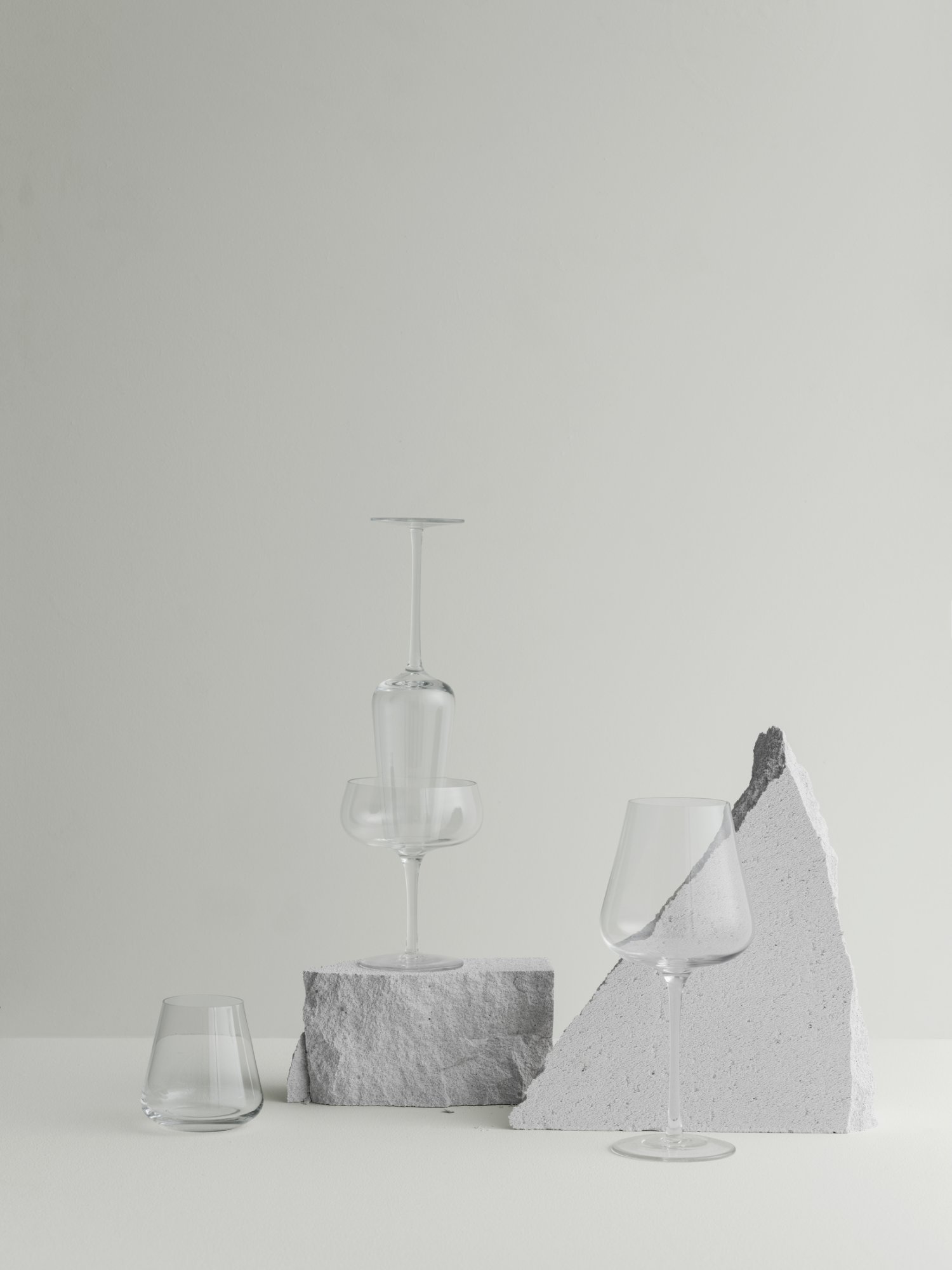 Elegantes Glasgeschirr, kunstvoll auf strukturierten Steinoberflächen vor einem minimalistischen Hintergrund arrangiert.