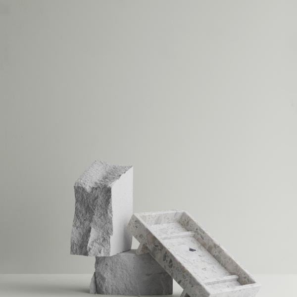 Moderne minimalistische Dekoration mit strukturierten Steinblöcken und einem Marmortablett auf hellem Hintergrund.