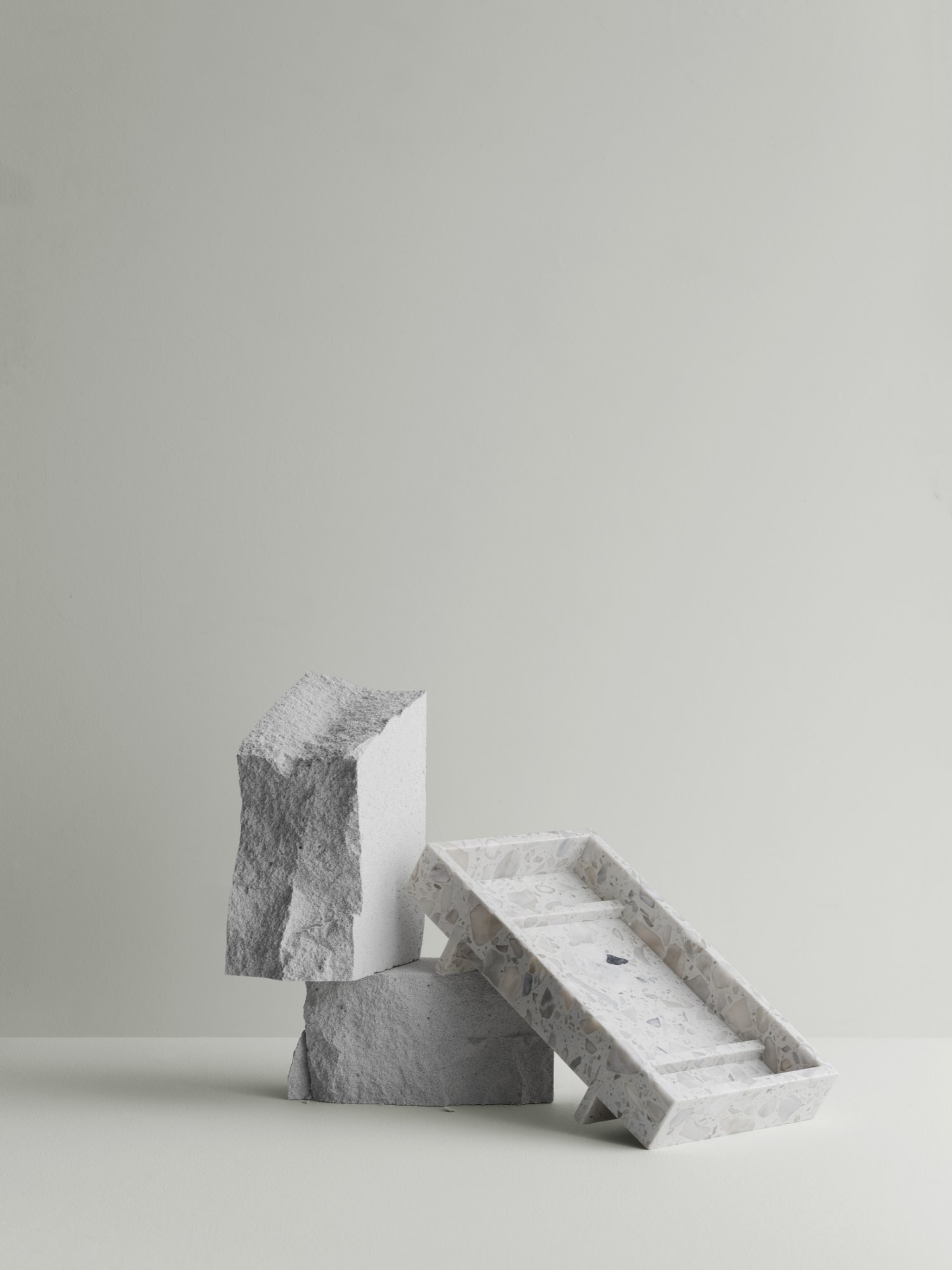Moderne minimalistische Dekoration mit strukturierten Steinblöcken und einem Marmortablett auf hellem Hintergrund.